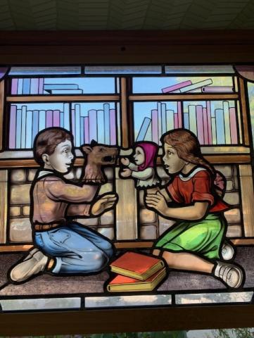 Stained glass image of children with books and puppets